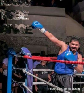 Coach Karthick in a Boxing ring, raising his right arm in a victory pose.