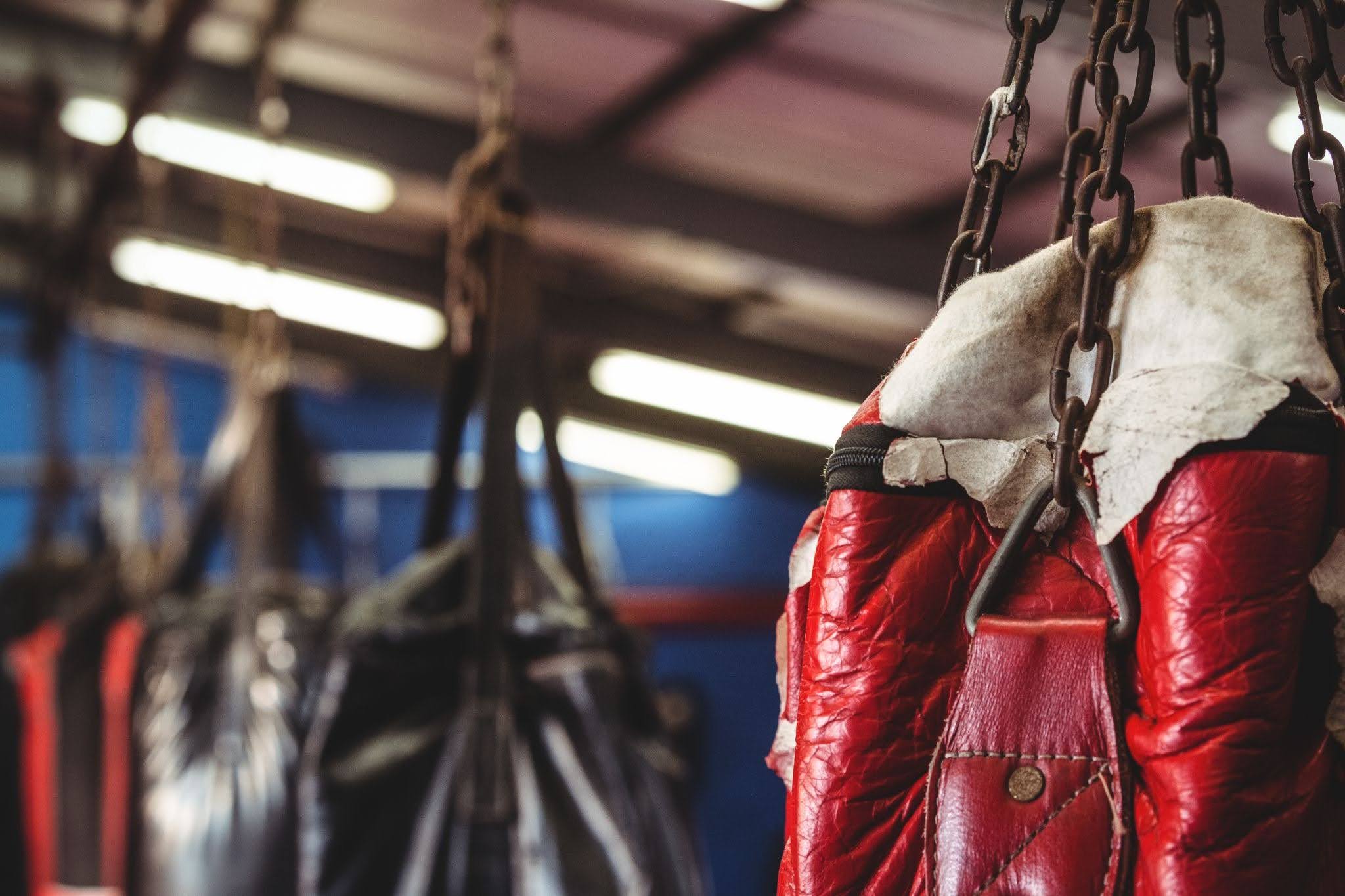 red leather punching bag hanging by metal chains in a boxing gym